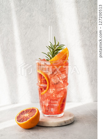 Blood orange cocktail with ice and rosemary on a marble stand on a gray background 127200513