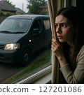 A woman looks out the window at a suspicious car parked outside 127201086