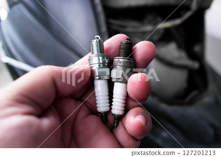 A hand holds two spark plugs comparison, one new and one used 127201213