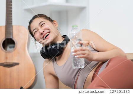 Joyful Hydration. Young woman laughing while holding water bottle after yoga workout. Joyful Hydration. Young woman laughing while holding water bottle after yoga workout. 127201385