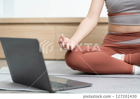 Yoga Focus and Meditation. Woman meditating at home with a laptop for guided yoga sessions. Yoga Focus and Meditation. Woman meditating at home with a laptop for guided yoga sessions. 127201430