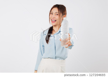 A young asian woman holds a plastic bottle with water, showing a smile as she prepares to drink the water in her hand for healthy hydration and refreshment, isolated studio white background 127204693