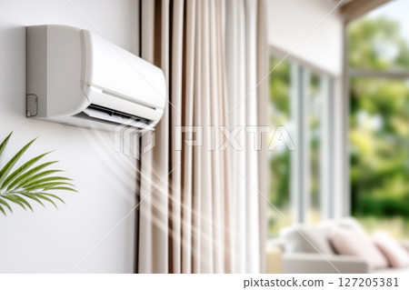 Air conditioning unit mounted on wall, providing cool air in modern living room with large windows and soft furnishings, enhancing indoor comfort 127205381