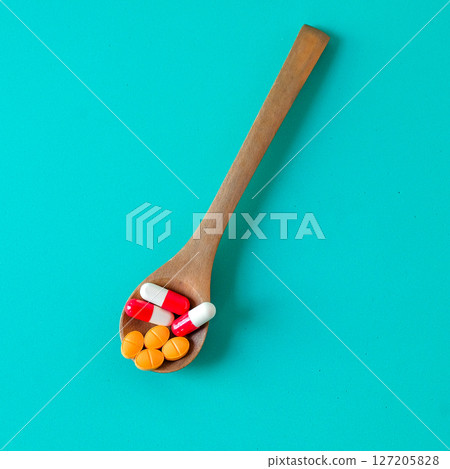 Medicine pills on wooden spoon over color background. 127205828