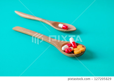 Medicine pills on wooden spoon over color background. 127205829