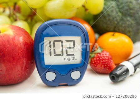 Asian hand holding digital glucose monitor measure with vegetable and fruit healthy food. 127206286