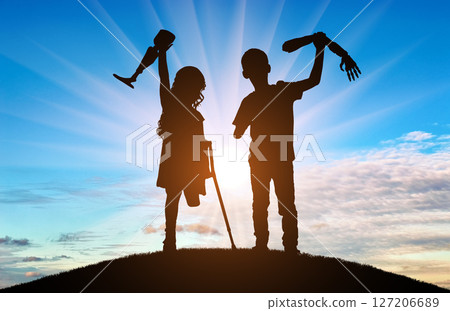 Two children silhouetted against a stunning sunset, proudly holding their prosthetic limbs Two children silhouetted against a stunning sunset, proudly holding their prosthetic limbs 127206689