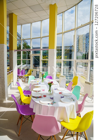 round tables served with dishes and white tablecloths with multi-colored chairs 127206728