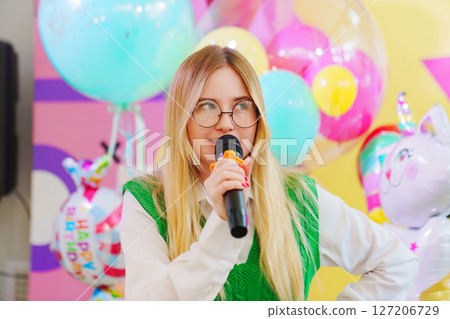 A funny young woman with a microphone is leading a children's party. 127206729