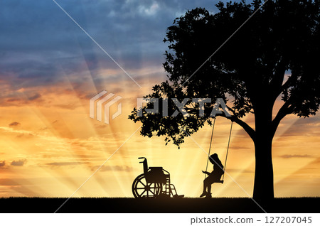 Girl schoolgirl invalid sitting on a swing under a tree, reading a book, beside a wheelchair 127207045