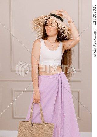 Attractive woman in summer outfit with straw hat and jute bag, perfect for vacation, beach or boho fashion shoots. 127208022