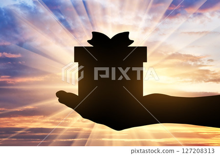 Altruism. Silhouette of a hand giving a gift on a sunset background 127208313