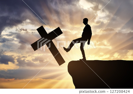 Man atheist pushes the symbol of christian cross into the cliff 127208424