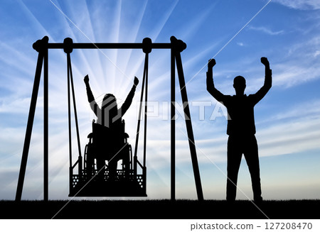Silhouette of a happy couple, a woman wheelchair user on an adaptive swing and a healthy man nearby. 127208470