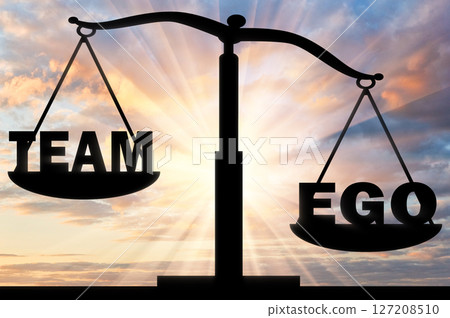 Silhouette of the scales of a bowl which is inclined towards the word ego against the backdrop of a sunset 127208510