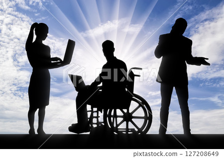 Inclusive Workplace Teamwork: Silhouettes of diverse professionals including a person in a wheelchair, working collaboratively on laptops against a vibrant sky. 127208649