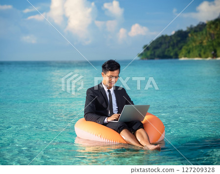 A male office worker in a suit relaxing on a swim ring floating in the sea 127209328