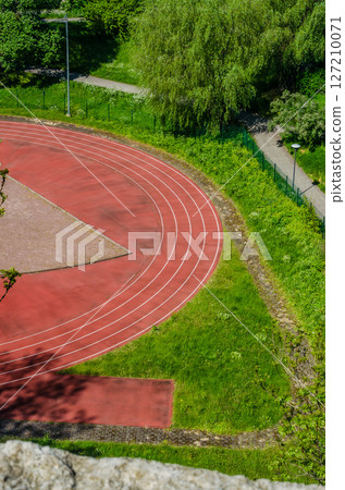 Curved red running track surrounded by grass and trees in summer. High quality photo 127210071