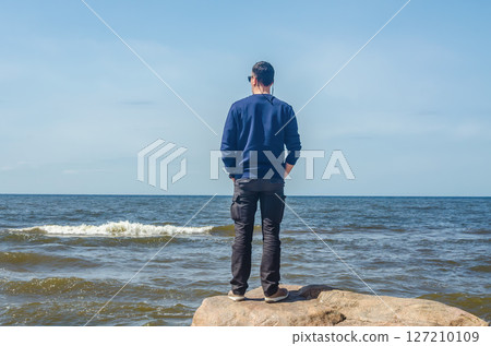 Man standing on rock looking at sea horizon under clear blue sky. High quality photo 127210109