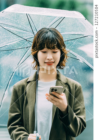 一名女子在雨中撐傘使用智慧型手機（雨季，六月） 127210584