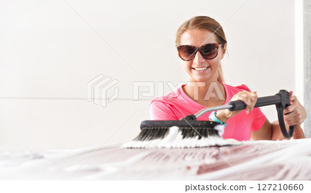 Young woman wearing pink t shirt and sunglasses cleaning her car in self serve carwash, photo with space for text left side 127210660