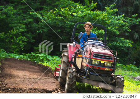Young man plowing the field with a tractor 127210847