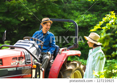 A man riding a tractor and a woman watching 127210925