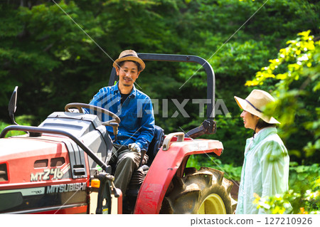 A man riding a tractor and a woman watching 127210926