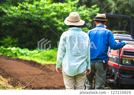 A man riding a tractor and a woman watching A man riding a tractor and a woman watching 127210929