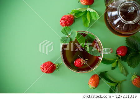 Bright strawberry tea in transparent glassware on a green background Bright strawberry tea in transparent glassware on a green background 127211319