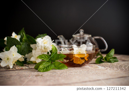 Fragrant tea with jasmine flowers in a glass cup on a black background 127211342