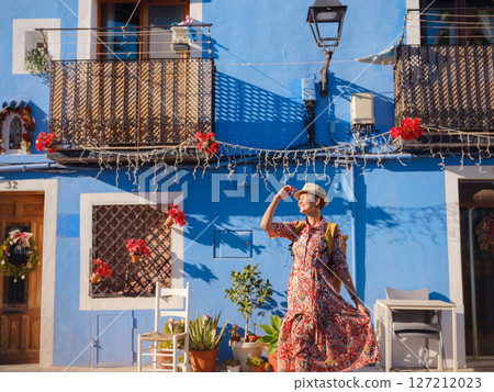 Woman in dress strolls through colorful streets of coastal town of La Vila Joiosa or Villajoyosa. Colorful homes in seaside villa of Villajoyosa in Southern Spain Woman in dress strolls through colorful streets of coastal town of La Vila Joiosa or Villajoyosa. Colorful homes in seaside villa of Villajoyosa in Southern Spain 127212023