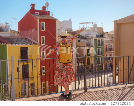 Woman in dress strolls through colorful streets of Spanish coastal town of La Vila Joiosa . sunny winter atmosphere highlights charm of Mediterranean architecture and quiet seaside life, back view 127212025