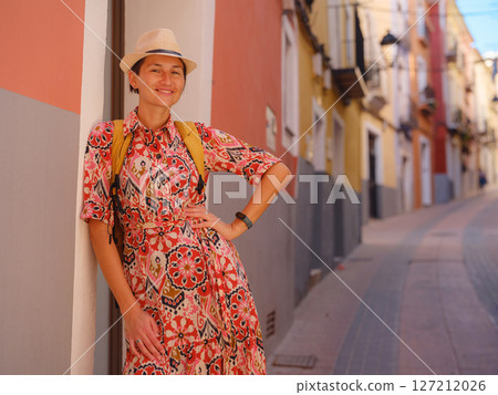 Woman in dress strolls through colorful streets of Spanish coastal town of La Vila Joiosa or Villajoyosa. sunny winter atmosphere highlights charm of Mediterranean architecture and quiet seaside life 127212026