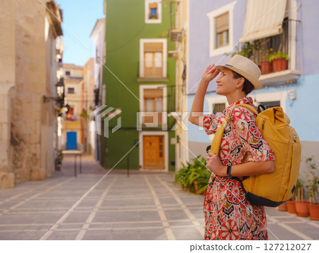 Woman in dress strolls through colorful streets of Spanish coastal town of La Vila Joiosa or Villajoyosa. sunny winter atmosphere highlights charm of Mediterranean architecture and quiet seaside life 127212027