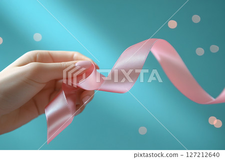 Young woman's hand holding a satin pink ribbon on a blue background. Generated by artificial intelligence 127212640