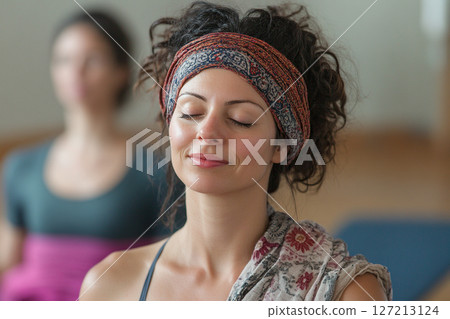 A serene woman sits in a calm yoga pose, her eyes softly closed as she enters a moment of deep relaxation and mindfulness. 127213124