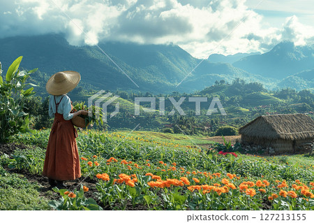 An Asian woman wearing a straw hat harvests crops in her vegetable garden overlooking rice paddies. Generated by artificial intelligence An Asian woman wearing a straw hat harvests crops in her vegetable garden overlooking rice paddies. Generated by artificial intelligence 127213155