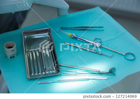 A Comprehensive Overview of Dental Instruments Arranged Neatly on a Blue Surgical Cloth in a Modern Dental Practice Setting with Bright Reflective Lighting 127214069