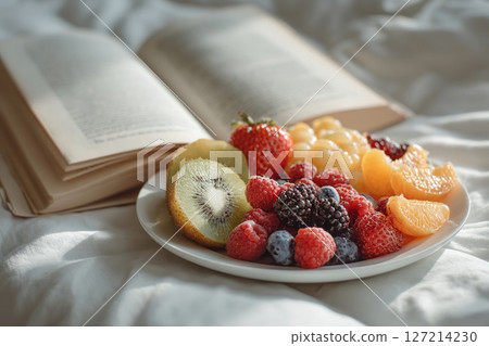 Plate of fresh fruit and open book on bed 127214230