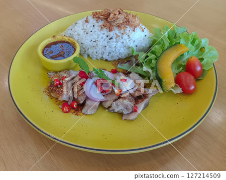 thai food, waterfall pork, fried garlic on rice and nam jim jaew in a yellow bowl, green vegetables, 1 piece of pumpkin, 2 tomatoes on a large yellow dish on a wooden background, food, copy space 127214509