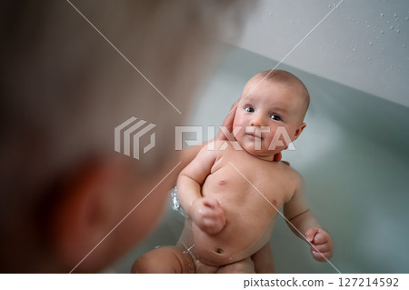 Top view cute baby bathing and swimming in the bath. Baby learning to swim and playing sports. Father enjoys bath time with his curious baby in a cozy bathroom. Fatherhood concept. Selective focus. 127214592