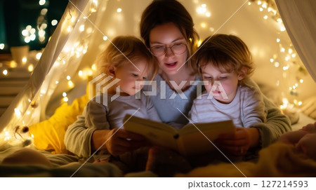 Mother reading a book to her children inside a cozy indoor fort decorated with fairy lights at night Mother reading a book to her children inside a cozy indoor fort decorated with fairy lights at night 127214593