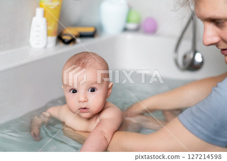 Cute baby bathing and swimming in the bath. Baby learning to swim and playing sports. Father enjoys bath time with his curious baby in a cozy bathroom. Fatherhood concept. Selective focus. Cute baby bathing and swimming in the bath. Baby learning to swim and playing sports. Father enjoys bath time with his curious baby in a cozy bathroom. Fatherhood concept. Selective focus. 127214598