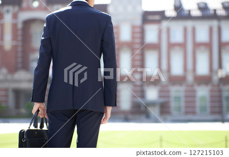 The back of a young businessman in a suit standing in a business district 127215103