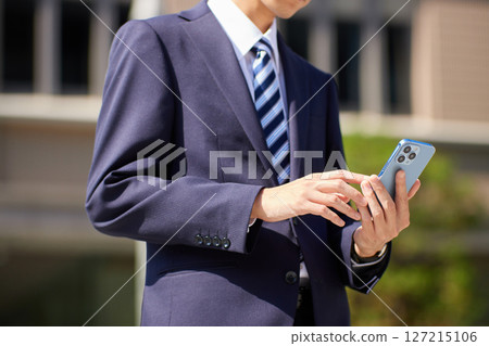 一位身著西裝的年輕商人在商業區看著智慧型手機 127215106
