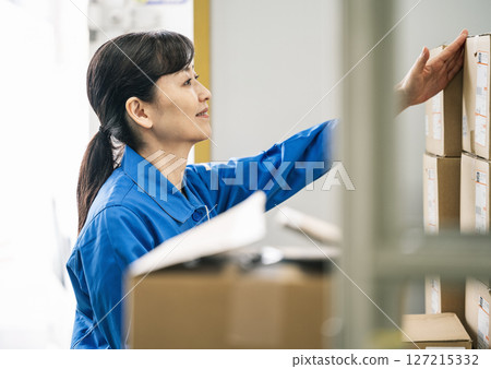 一名身穿工作服的 50 多歲女性在物流倉庫工作 127215332