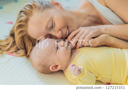 Mother and baby lying on a play mat. Tender bonding moment, cozy childhood atmosphere, and early development. Parenting, love, and infant care concept Mother and baby lying on a play mat. Tender bonding moment, cozy childhood atmosphere, and early development. Parenting, love, and infant care concept 127215351