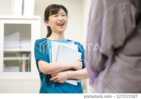 A woman in her 50s happily talking with her colleagues in the office 127215387