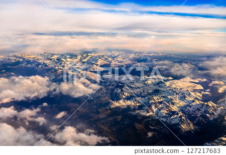 Aerial view of the snow-covered Sierra Nevada mountains in California during sunset, revealing dramatic peaks and rugged terrain with golden light highlighting the landscape 127217683